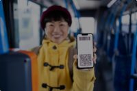Smiling woman showing an eSIM activation QR code on a bus, highlighting Valid's seamless digital activation experience without a physical SIM card.